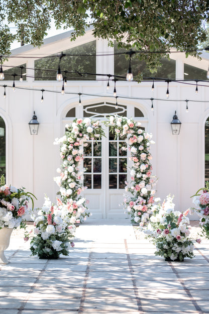pink and white wedding setup with arch, aisle meadows and urns in outdoor garden setting