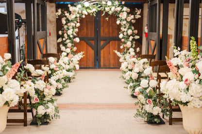 Lush pink and white Blushing Bride arch and aisle flowers in indoor ceremny setting