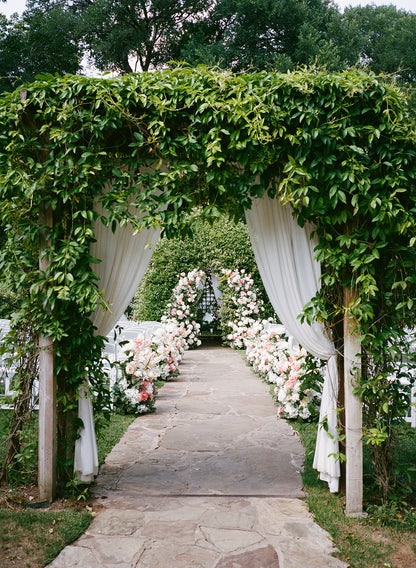 Decorative archway with greenery and floral arrangements on a stone path