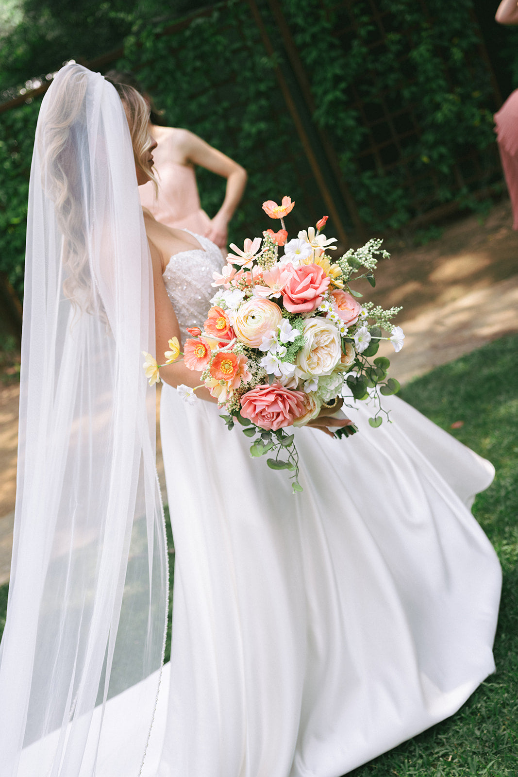 Bride holding a bouquet of flowers with a long veil, standing outdoors.