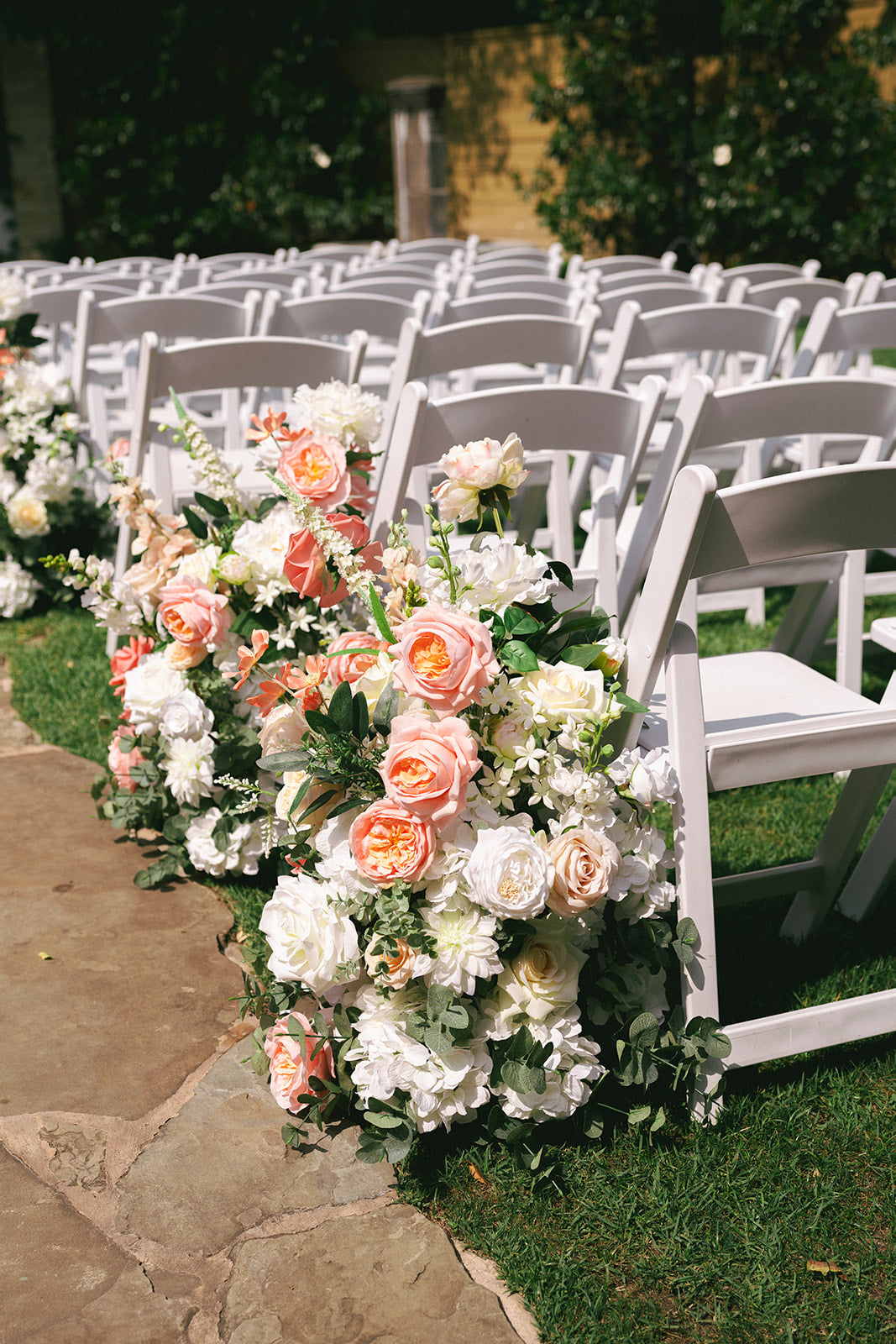 Decorative floral arrangements on white chairs at an outdoor wedding venue.