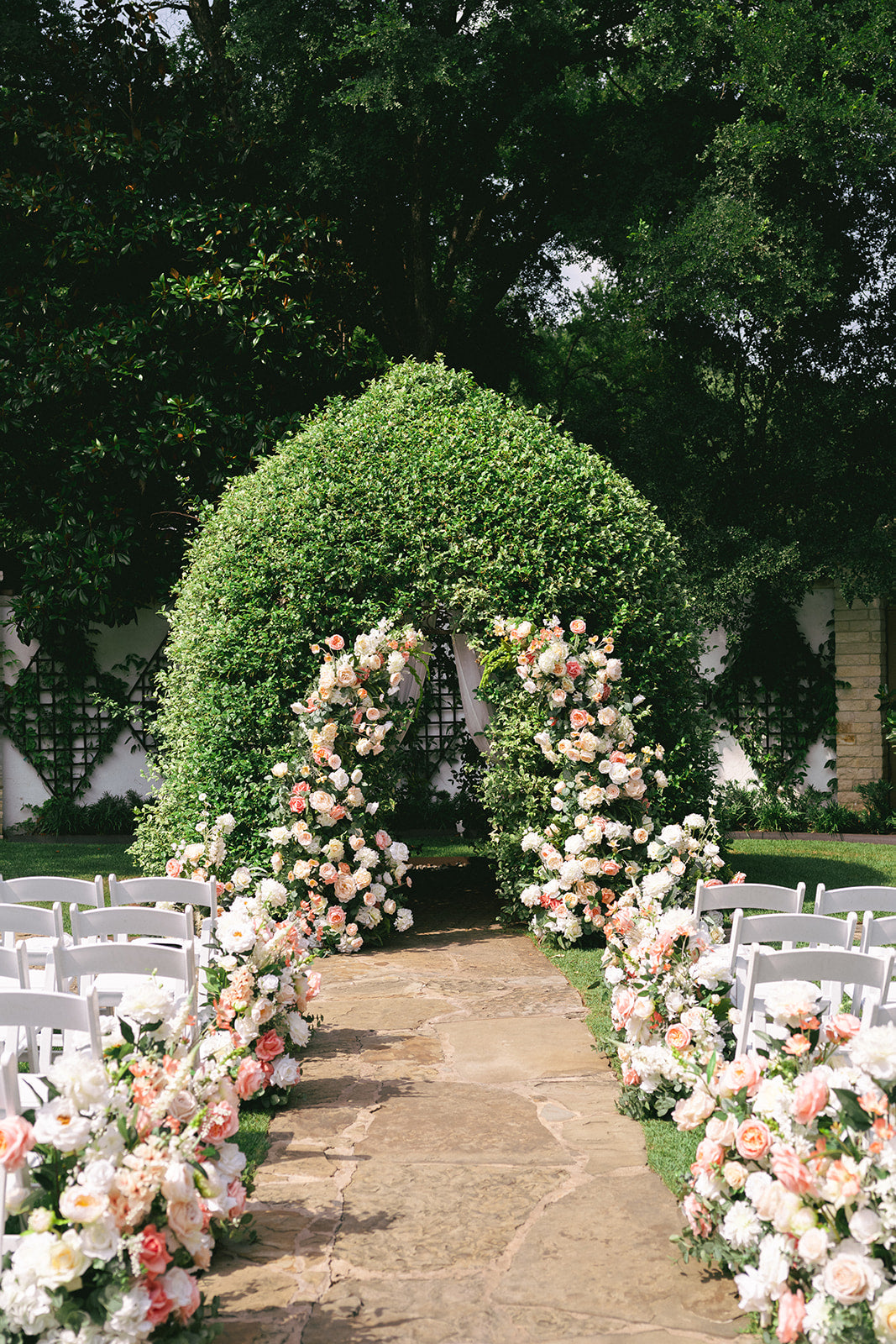Floral archway at a wedding ceremony site with greenery and white chairs.